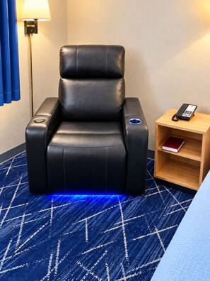 A black massage chair with a control panel, a bedside table with a phone, and a patterned blue carpet. - Super 8 by Wyndham Hot Springs (Hot Springs)