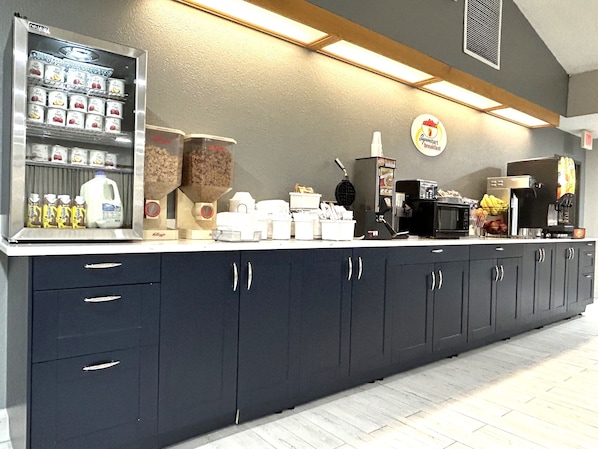 A breakfast bar with a refrigerator stocked with beverages, a waffle maker, and a coffee machine. - Super 8 by Wyndham Hot Springs (Hot Springs)