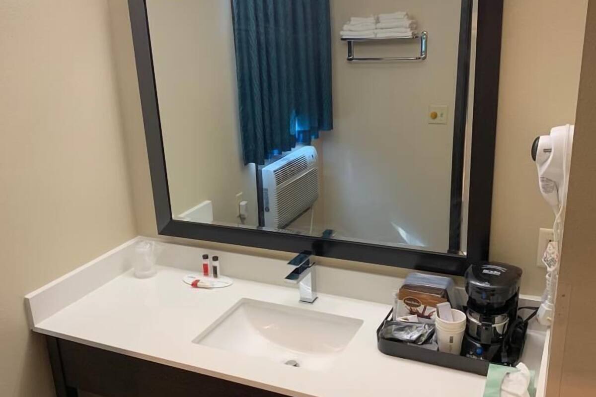 A hotel bathroom with a large mirror, white sink, and a coffee maker on the counter.