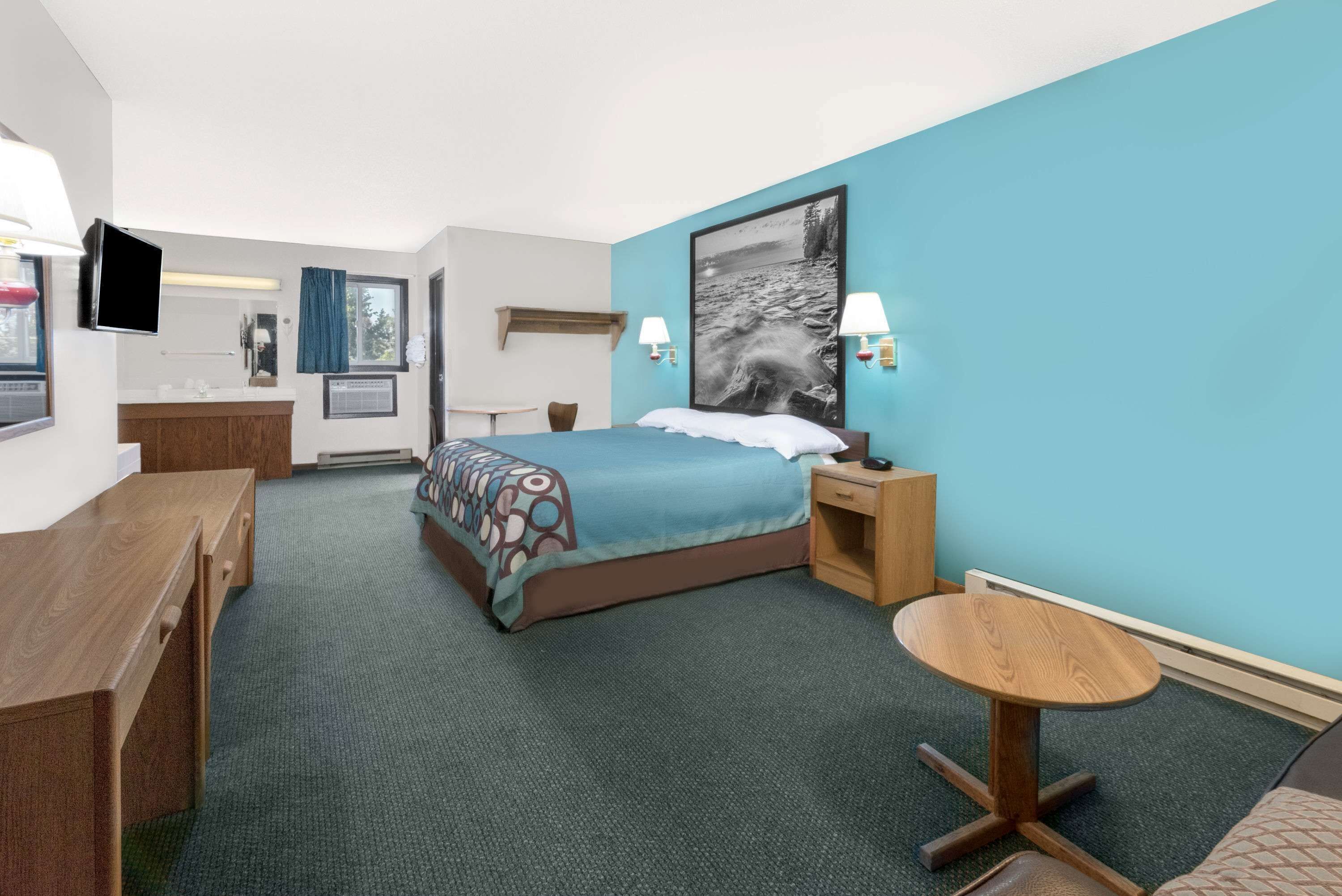 A hotel room with a bed, bedside table, lamp, and a small round table.