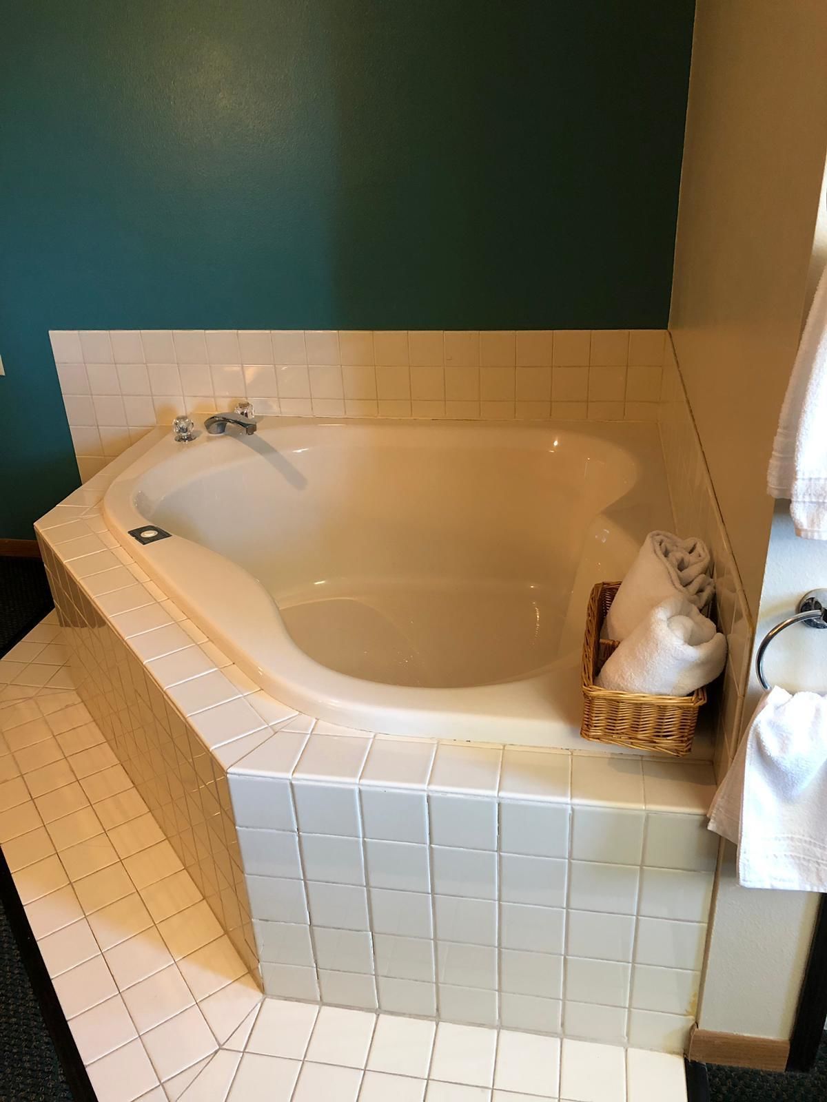 Une salle de bain avec une baignoire sur pieds, des murs recouverts de carreaux blancs et un panier en osier contenant des serviettes.