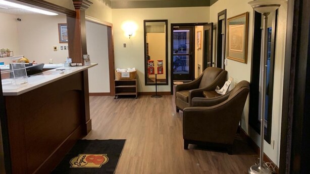 Zona de recepción con mostrador, un sillón de cuero marrón, una lámpara de pie y una puerta que da al exterior.