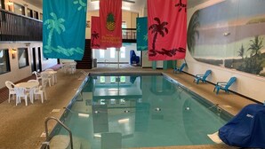 Una piscina interior con barrera de cristal, rodeada de sillas y mesas blancas.