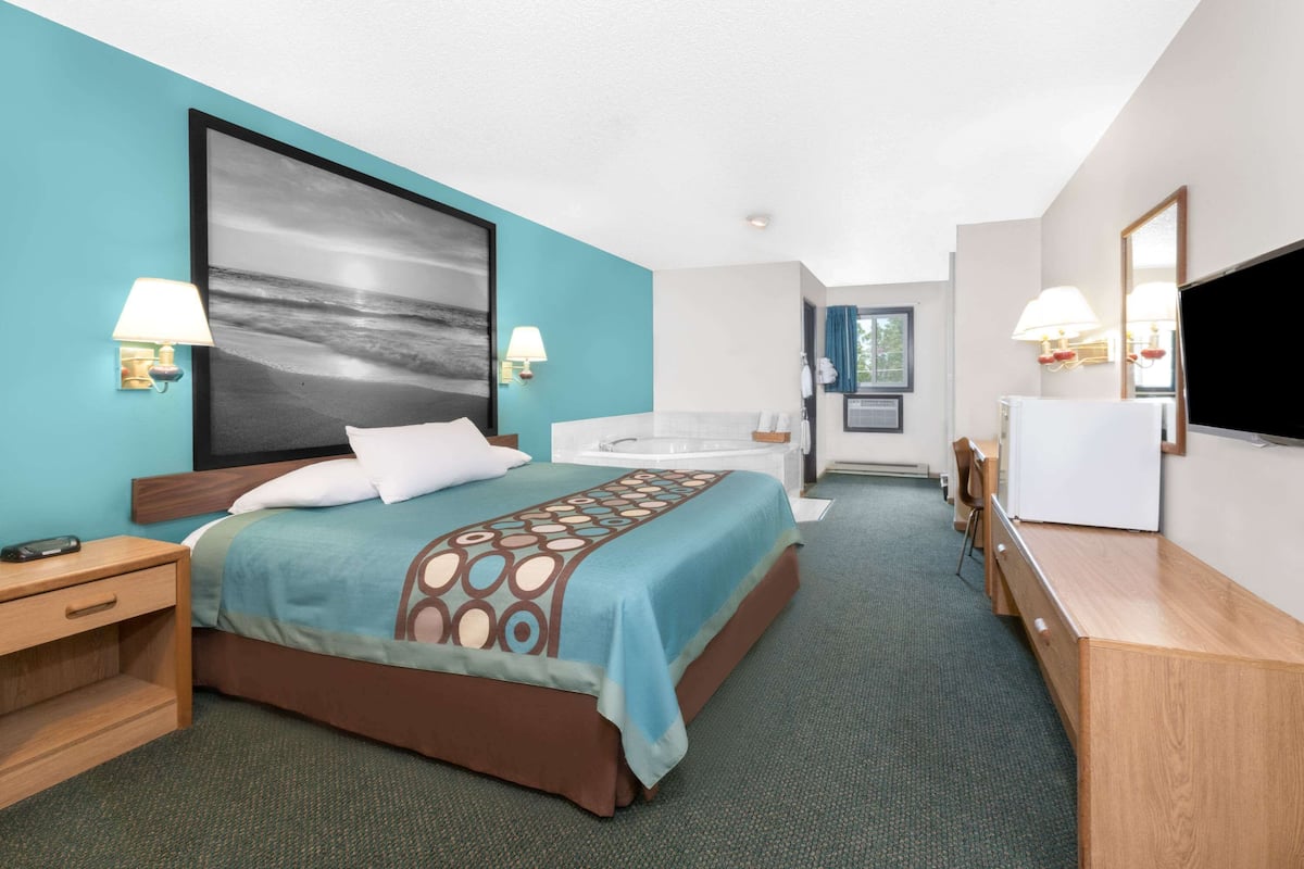 A hotel room with a bed, a desk, a chair, a bathtub, and a TV.