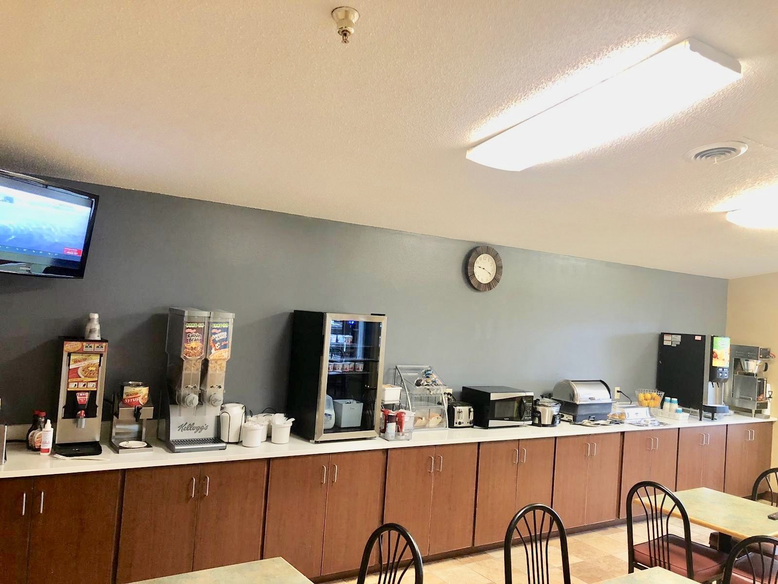 A breakfast bar with a coffee machine, a microwave, and a refrigerator. There are wooden cabinets below and a clock on the wall.