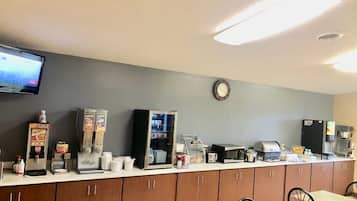 A breakfast bar with a coffee machine, a microwave, and a refrigerator. There are wooden cabinets below and a clock on the wall.