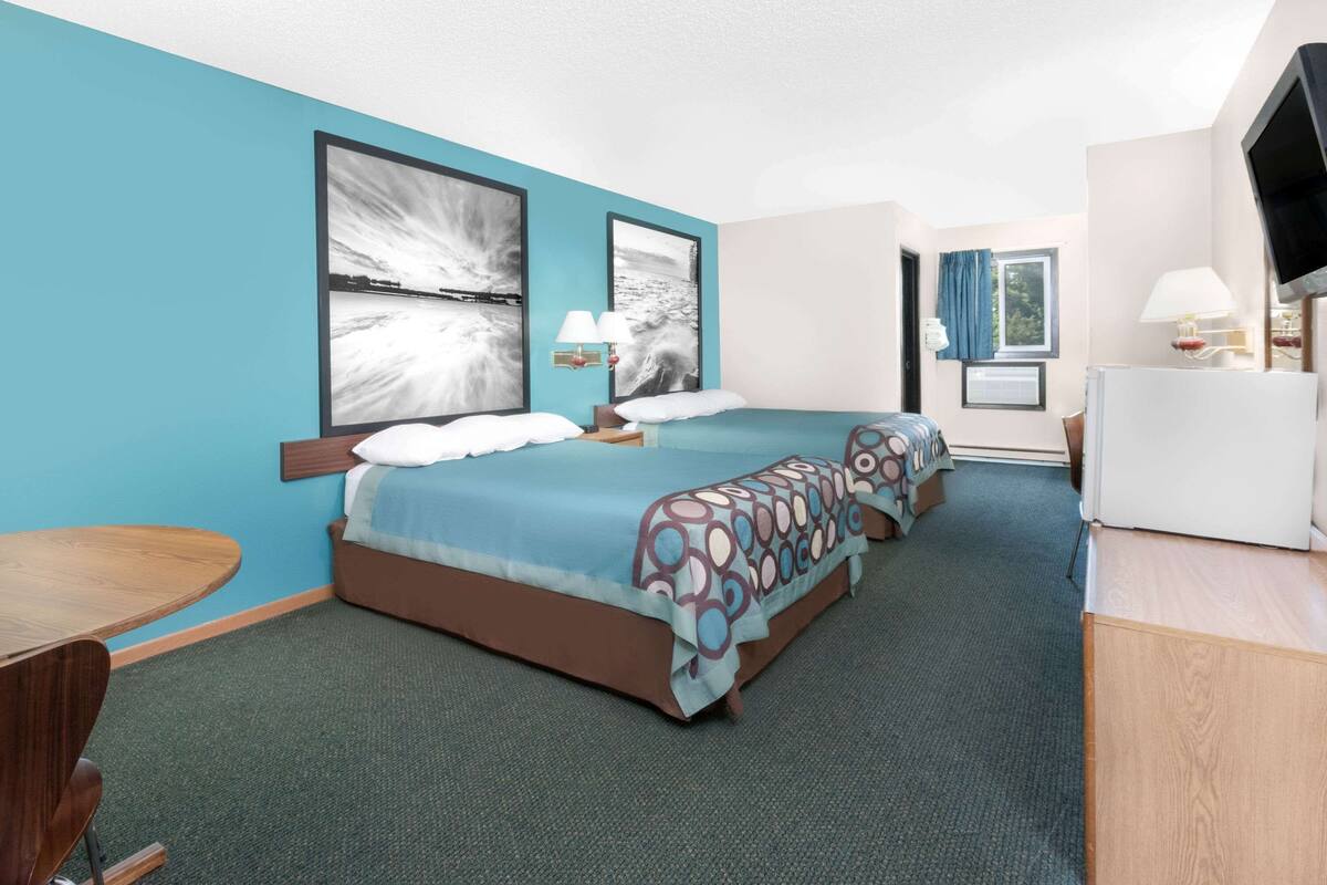 A hotel room with two beds, a desk, a TV, and artwork on the walls.