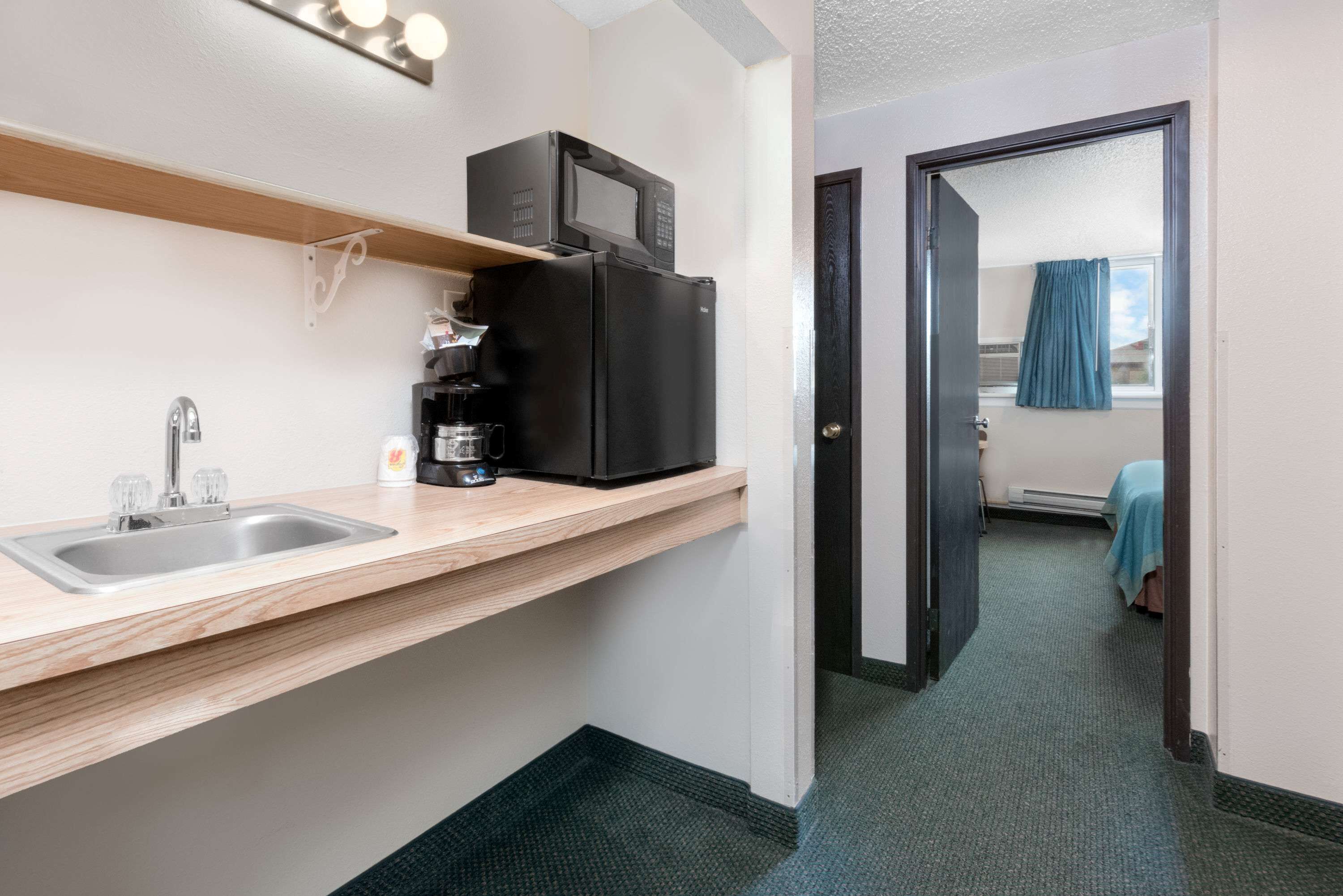 A compact kitchen with a sink, a coffee maker, and a microwave on a shelf.