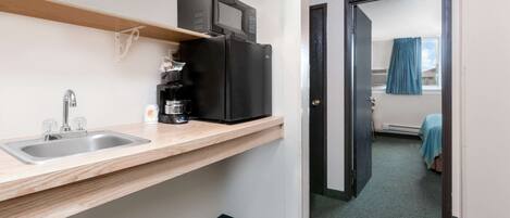 A compact kitchen with a sink, a coffee maker, and a microwave on a shelf.