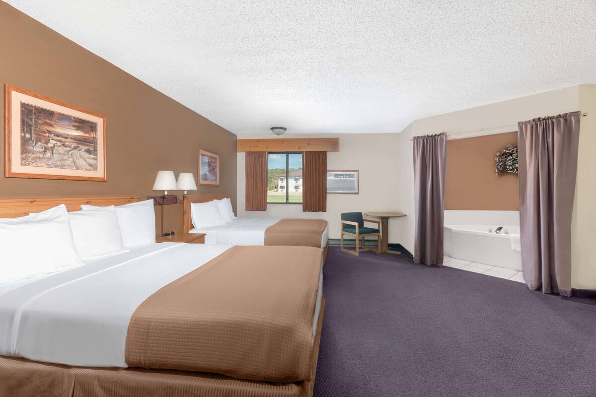 A hotel room with two beds, a desk, a chair, a window with curtains, a painting on the wall, and a bathtub.