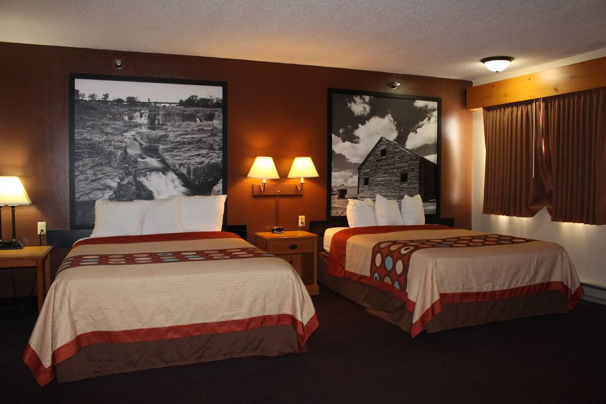 A hotel room with two beds, a nightstand, a lamp, and two wall-mounted lamps.