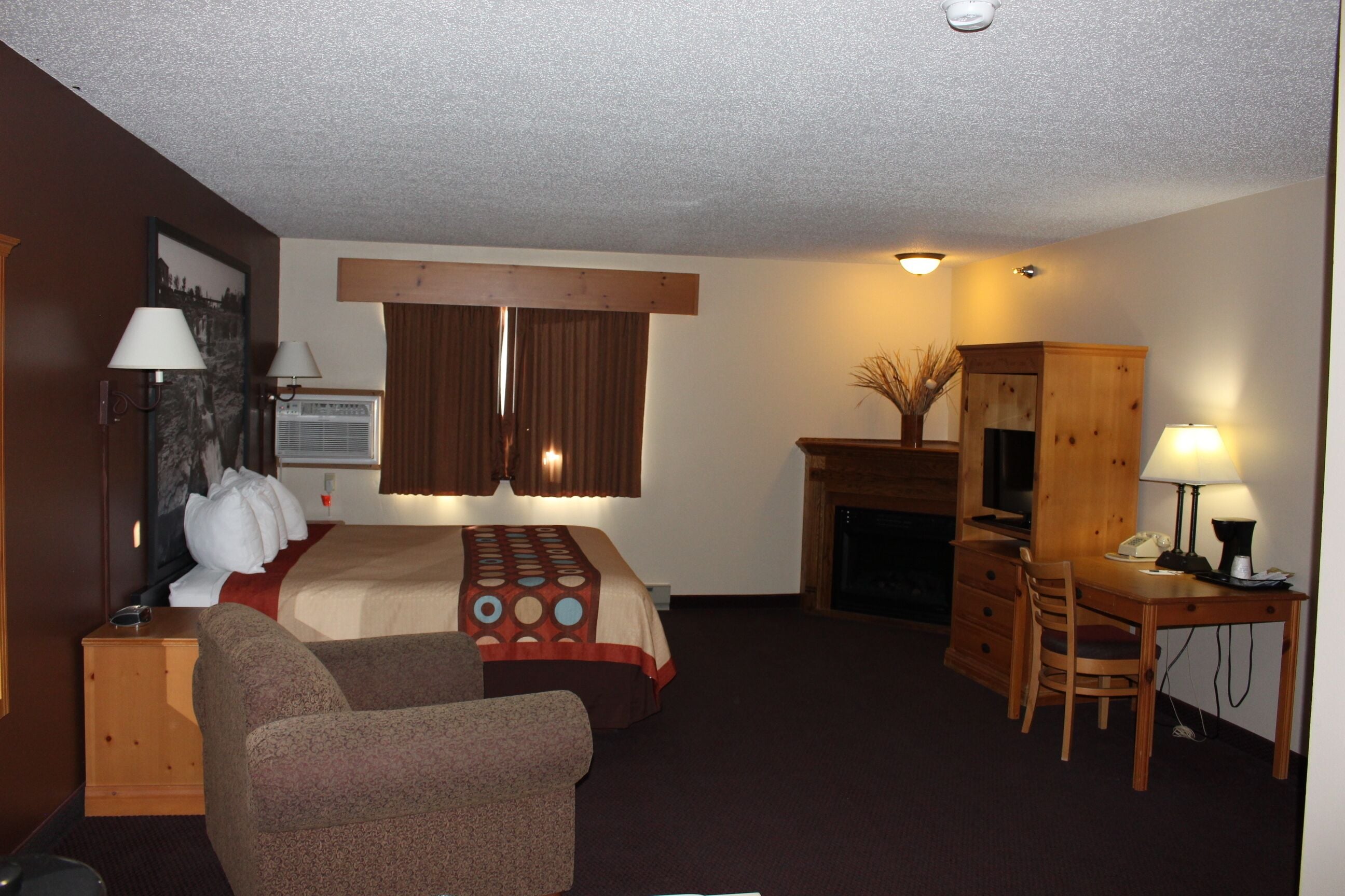 Hotelkamer met een bed, bureau, stoel, lamp, open haard en een schilderij aan de muur.