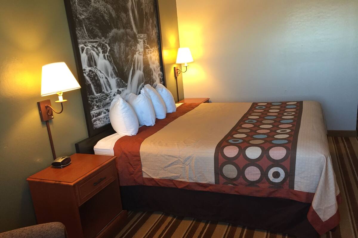 A hotel room with a bed, two bedside lamps, a nightstand, a telephone, and a large wall painting.