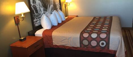 A hotel room with a bed, two bedside lamps, a nightstand, a telephone, and a large wall painting.