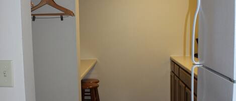 A compact kitchen with a refrigerator, a wooden chair, and a hanging coat rack.