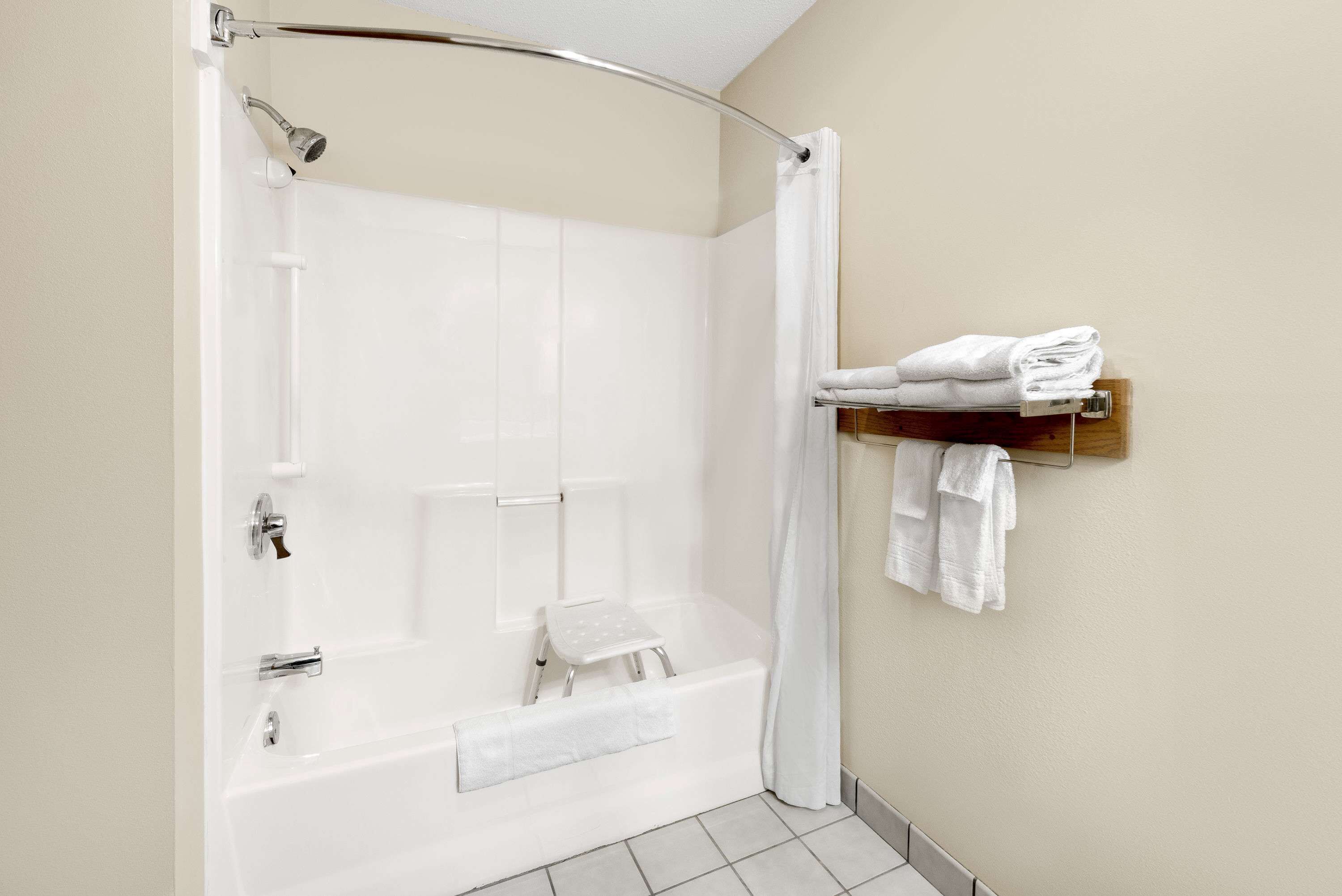 Un baño moderno con ducha a ras de suelo, asiento integrado y un perchero con toallas dobladas.