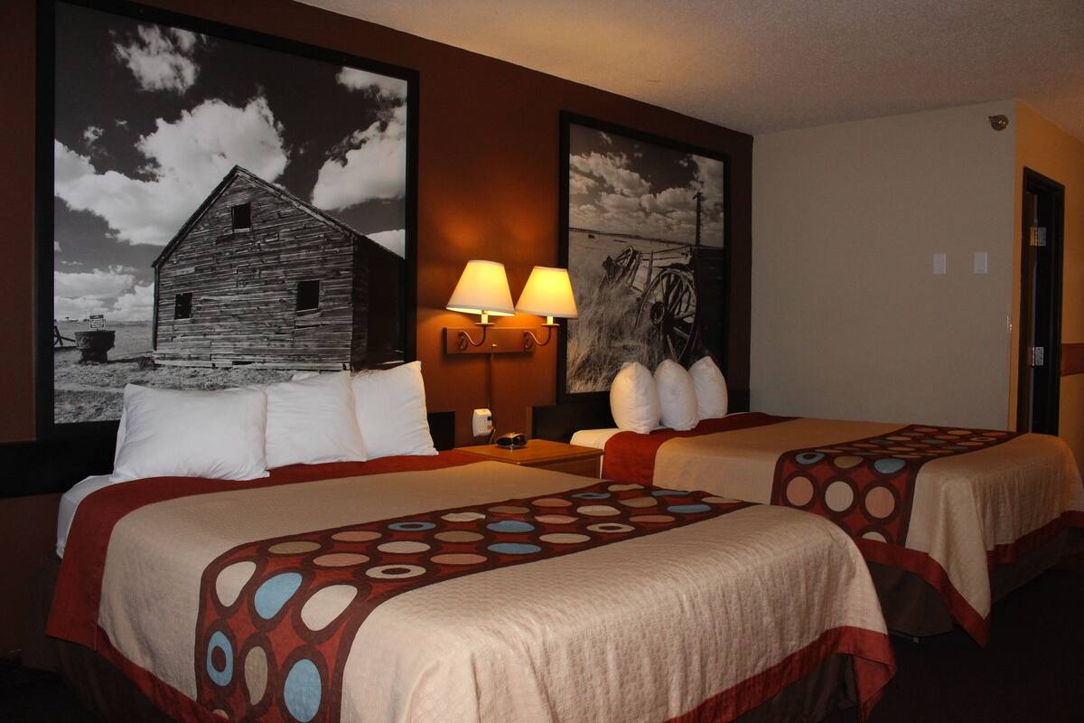 A hotel room with two beds, each with a patterned bedspread, a nightstand with a lamp, and two wall-mounted lamps.