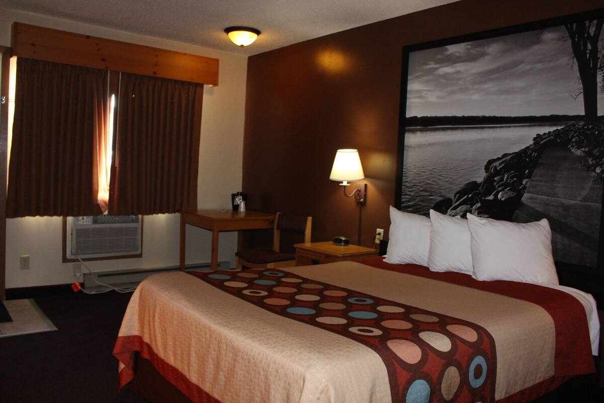 A hotel room with a large bed, a desk, a chair, a lamp, and a view of a lake.
