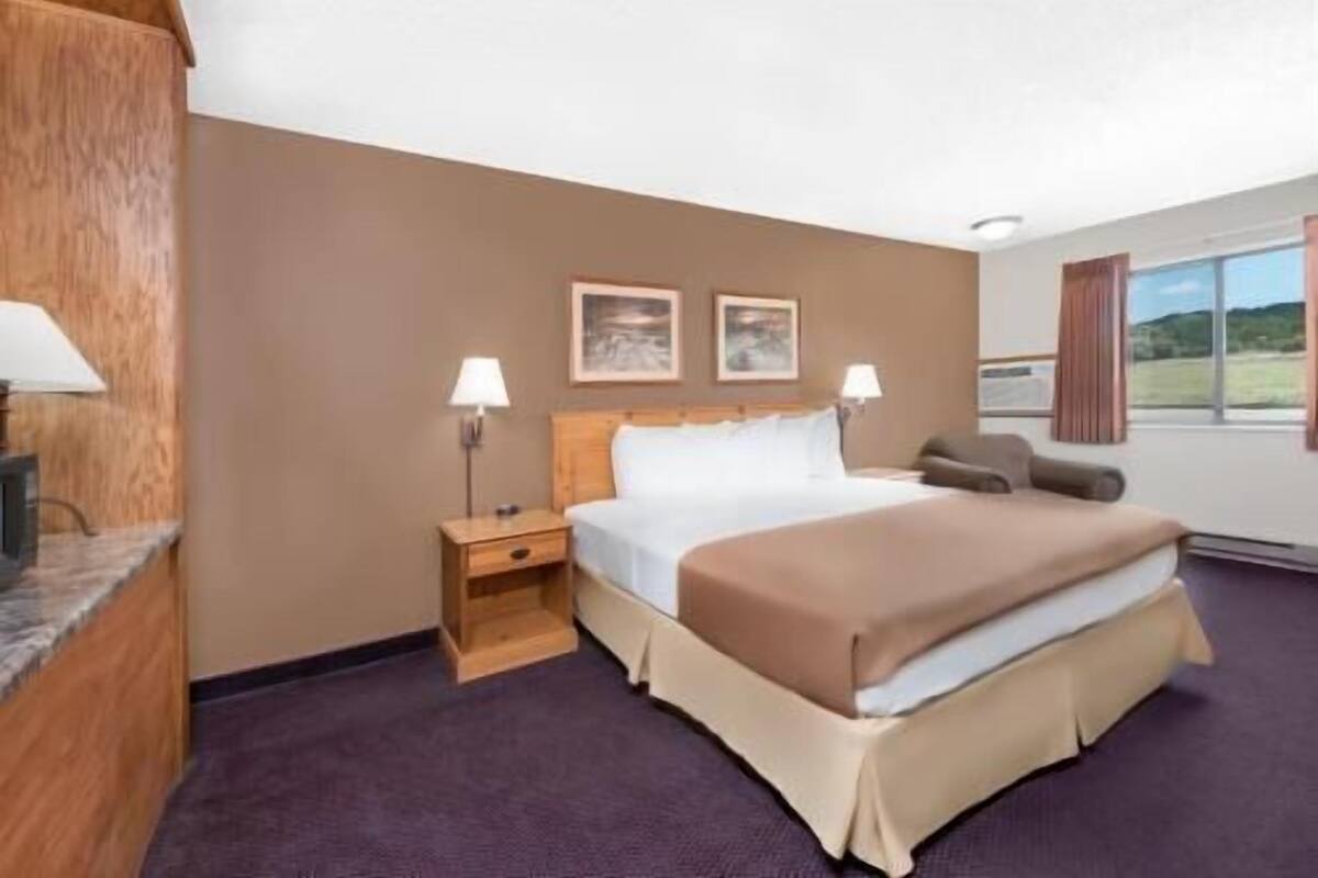 A hotel room with a bed, two bedside lamps, a nightstand, a chair, and a window with a view.