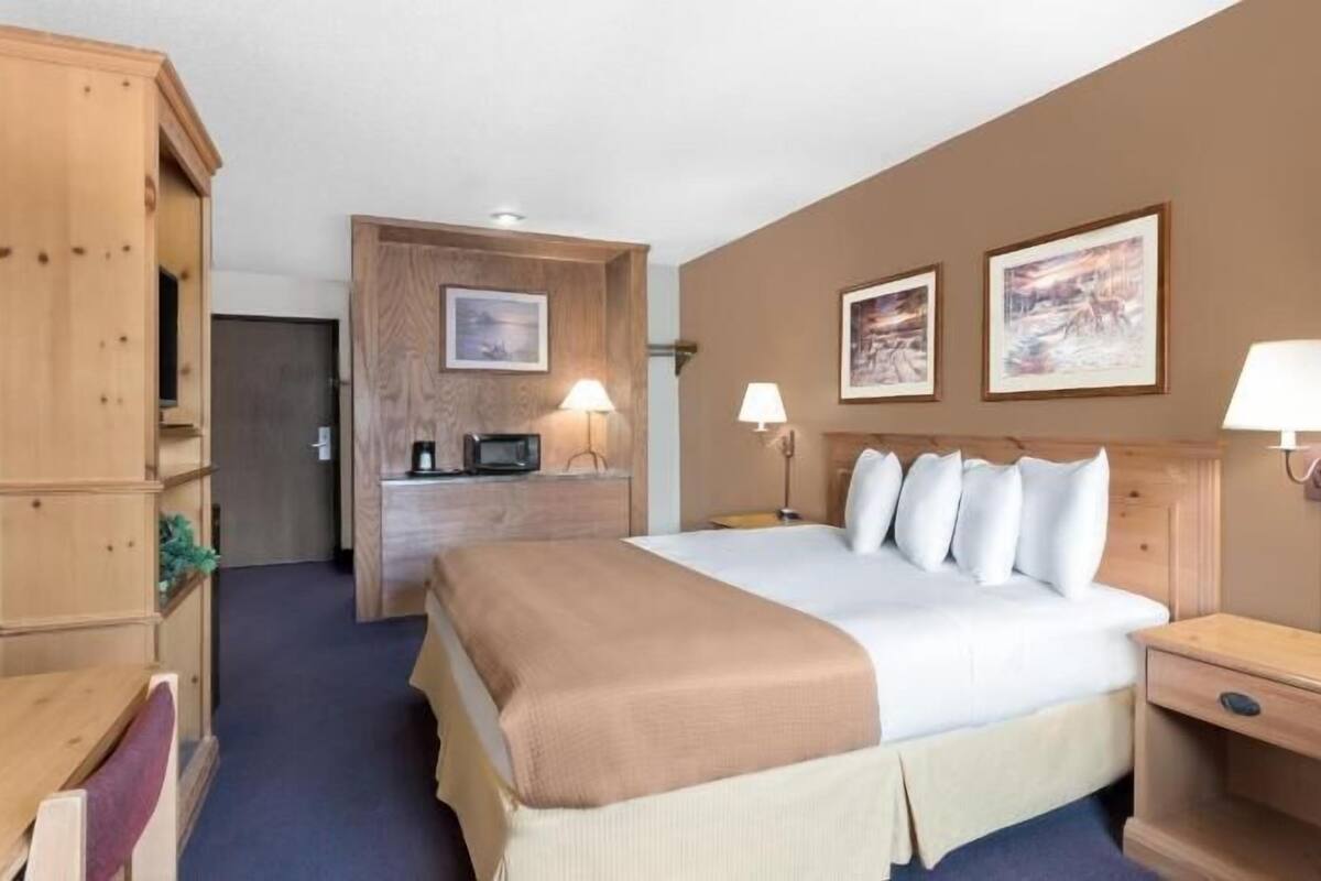 A hotel room with a bed, bedside tables, a desk with a chair, a wardrobe, and two wall-mounted lamps.