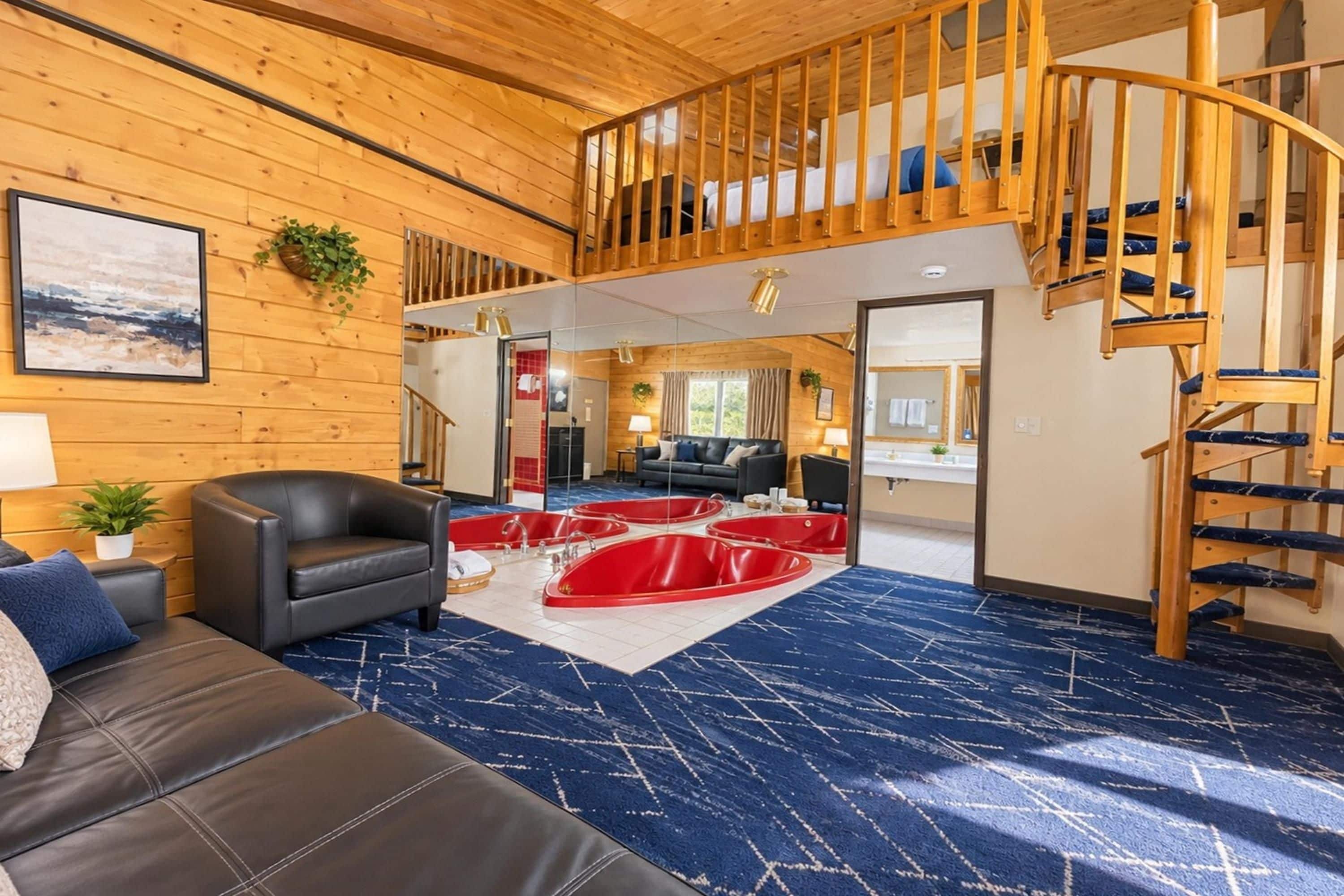 A spacious living area with a black leather sofa, red bathtubs, and a wooden staircase.