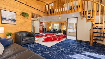 A spacious living area with a black leather sofa, red bathtubs, and a wooden staircase.