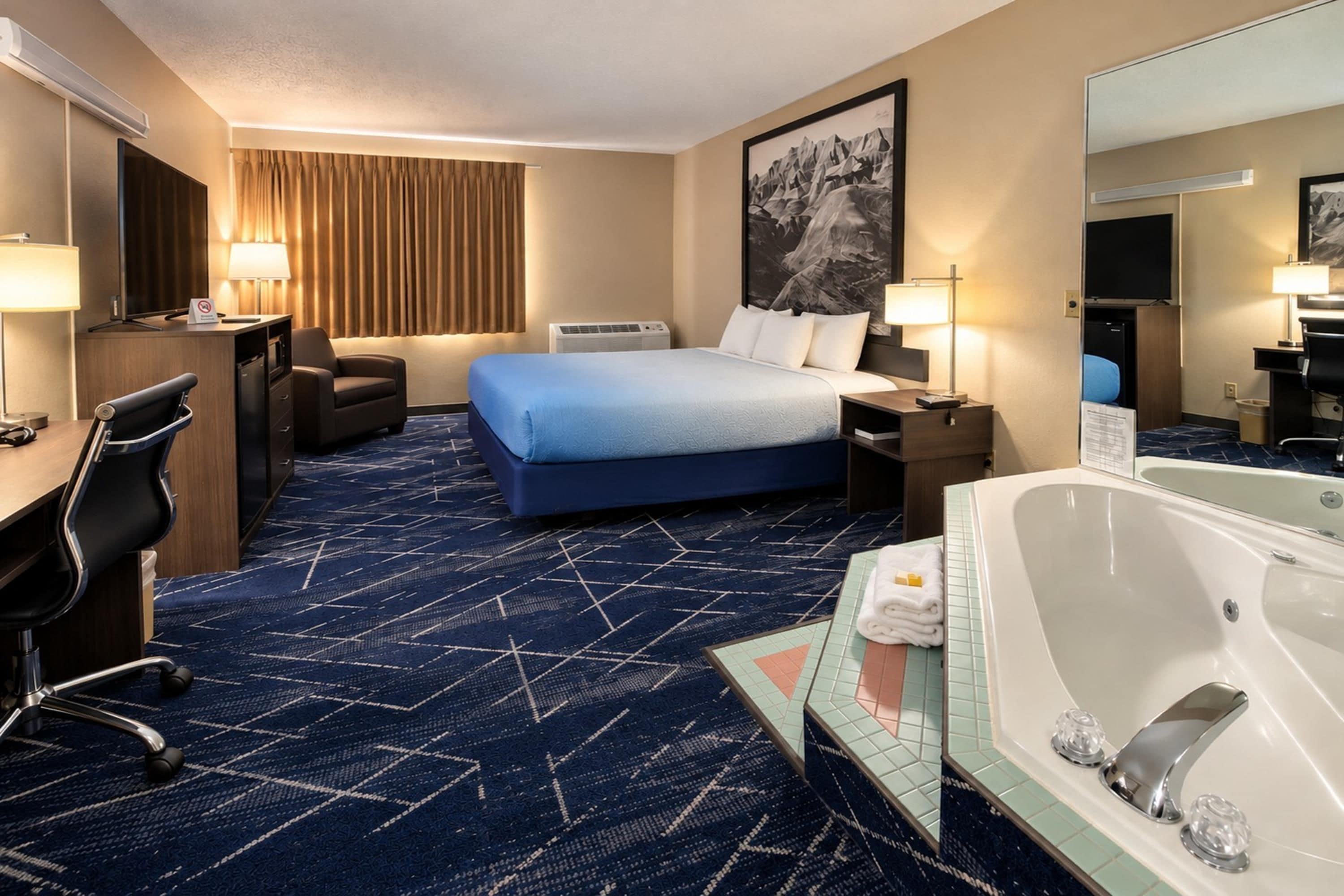 Une chambre d’hôtel comprenant un lit, un bureau, une chaise et une salle de bain avec baignoire.