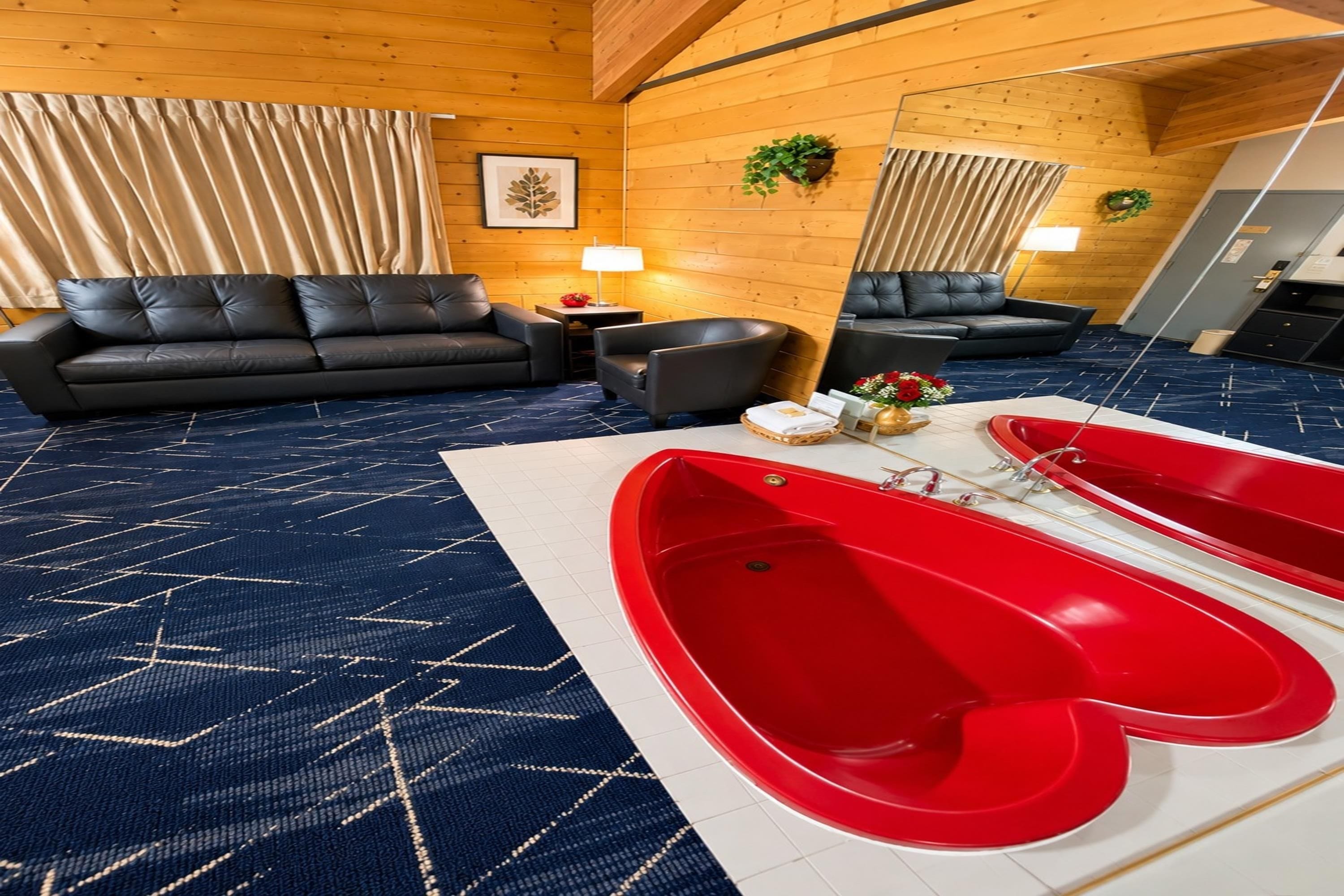 A room with a black leather sofa, a small table with a lamp, a red bathtub, and a blue patterned carpet.