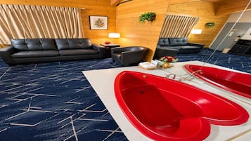 A room with a black leather sofa, a small table with a lamp, a red bathtub, and a blue patterned carpet.