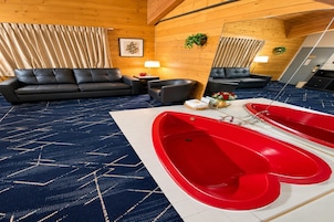 Una habitación con un sofá de cuero negro, una mesita con una lámpara, una bañera roja y una alfombra azul estampada.
