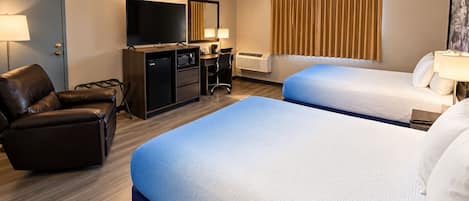 Habitació d'hotel amb dos llits, una taula, una cadira, una televisió i una finestra amb cortines.