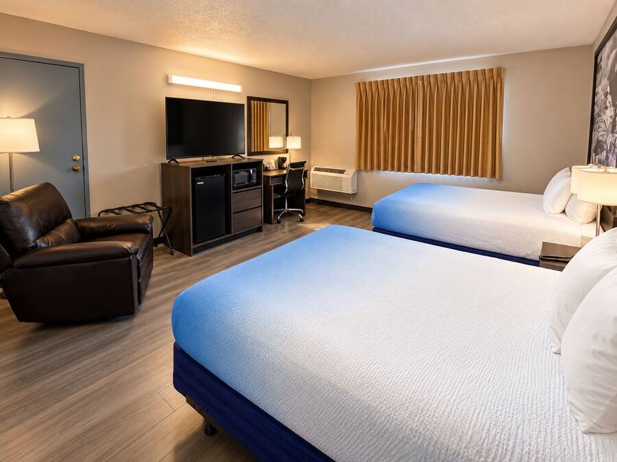 Ein Hotelzimmer mit zwei Betten, einem Schreibtisch, einem Sessel, einem Fernseher und einem Fenster mit Vorhängen.