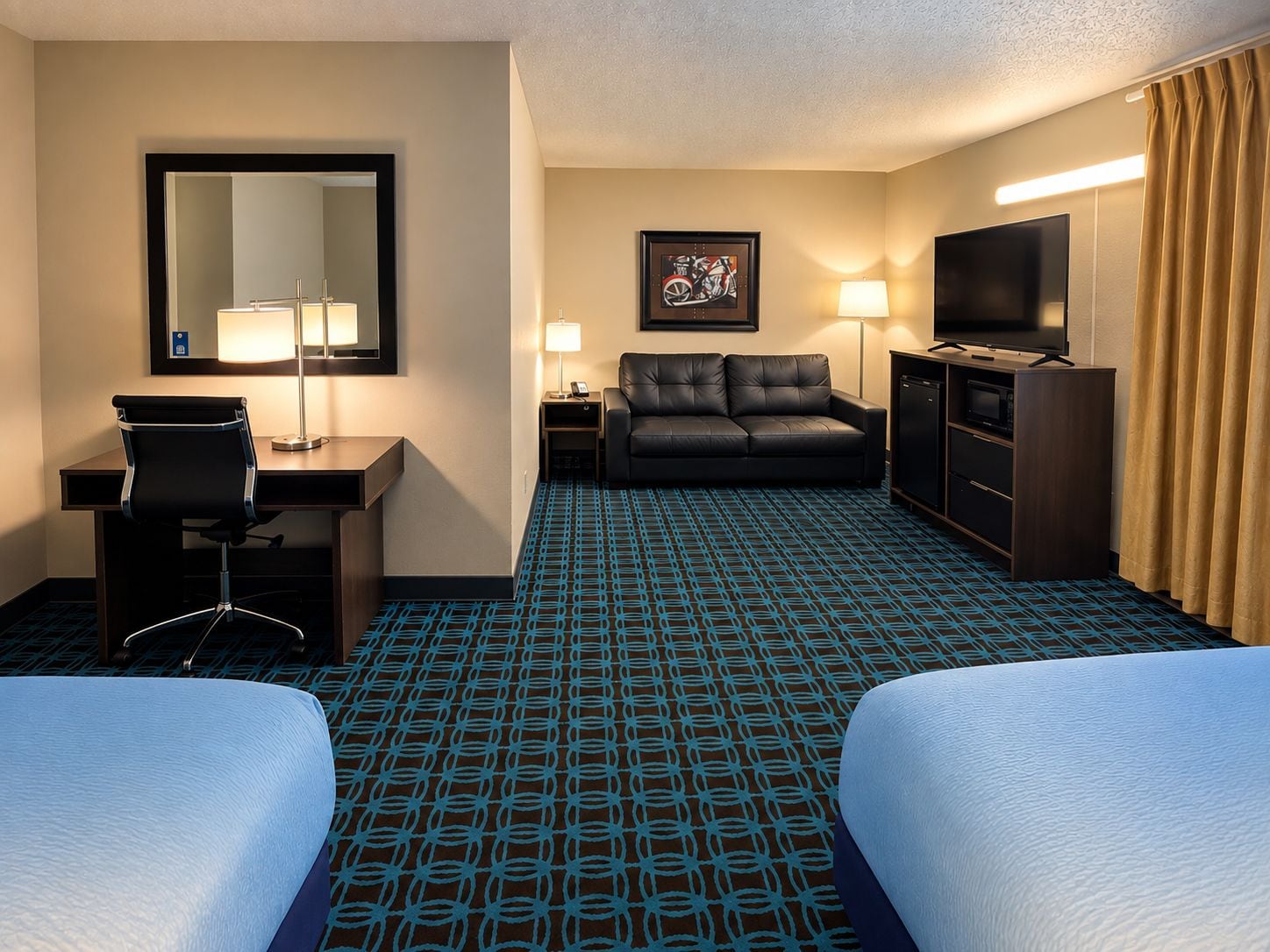 Une chambre d’hôtel équipée d’un bureau, de deux lits, d’un canapé, d’une télévision et d’une moquette à motifs.