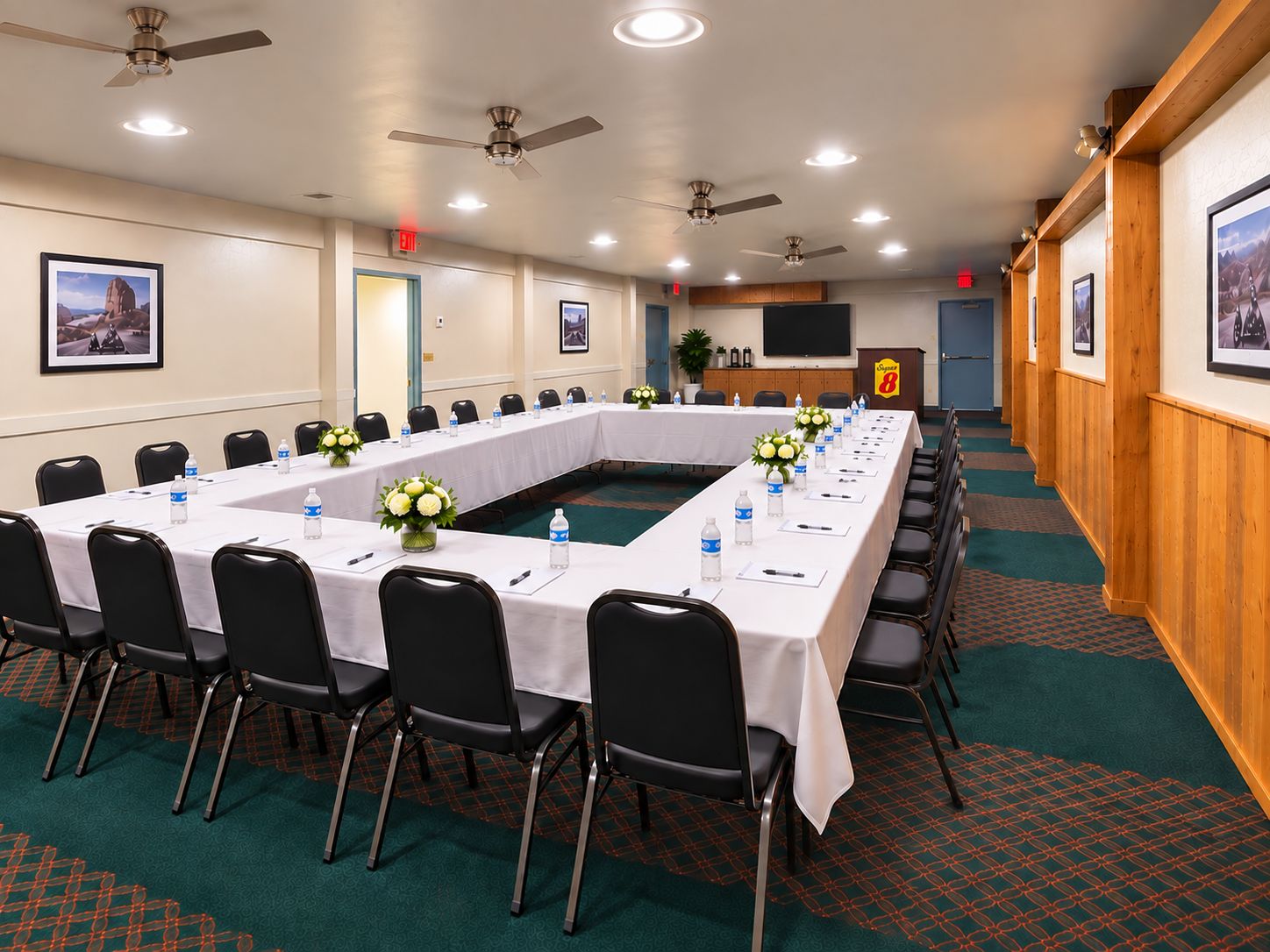 A conference room with a long table, chairs, ceiling fans, and framed pictures on the walls.