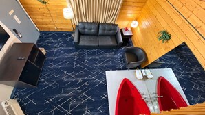 A room with a sofa, a chair, a small table, a red bathtub, and a blue patterned floor.