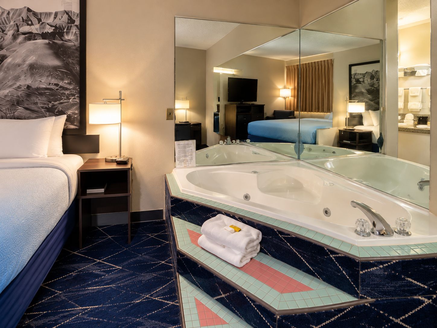 Een hotelkamer met een bed, een grote spiegel, een badkuip en een televisie.