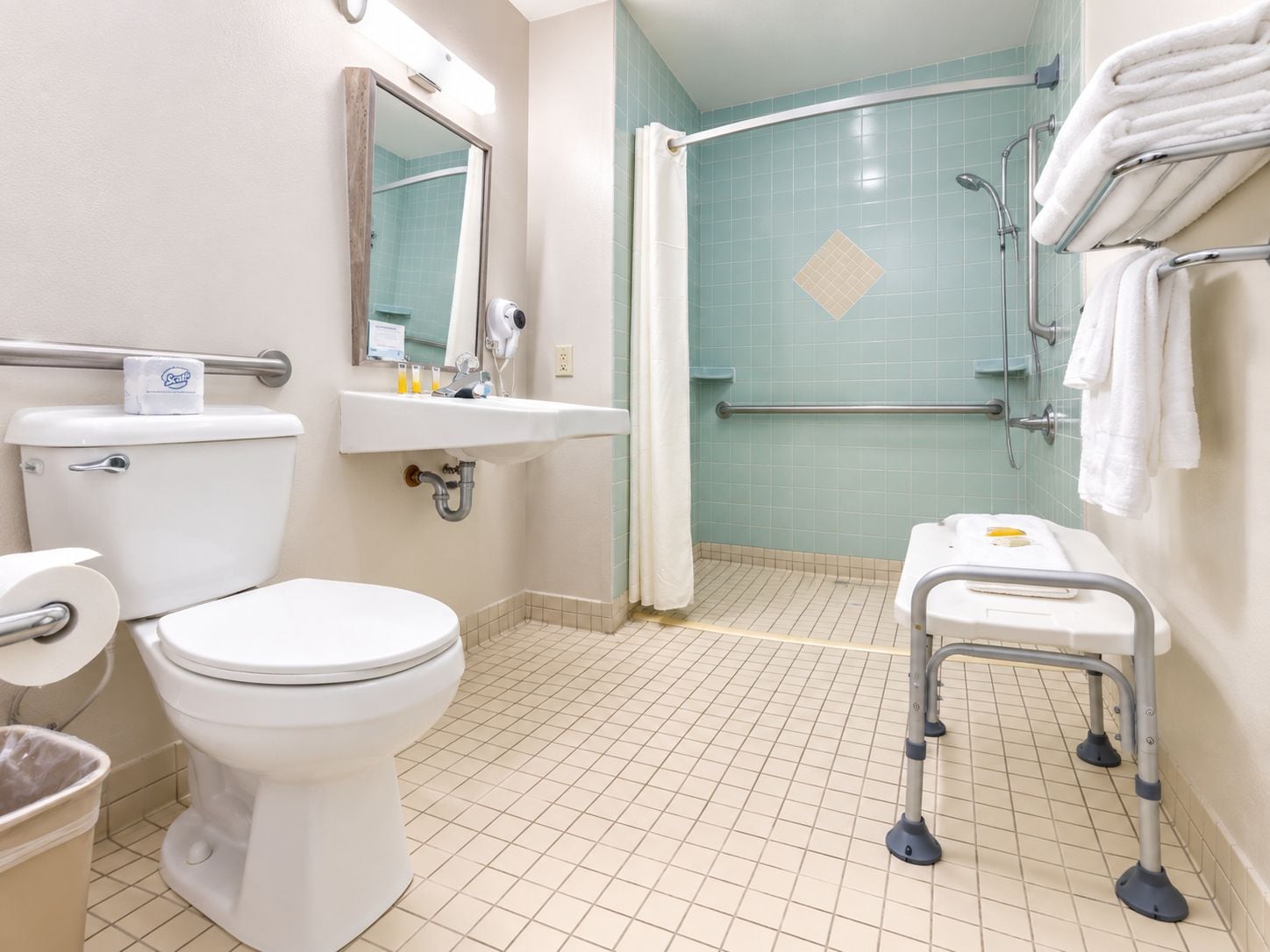 A bathroom with a toilet, sink, shower, and grab bars.