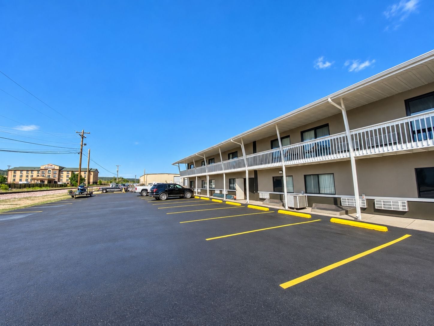 Un motel con estacionamiento, un edificio de dos pisos y un cielo azul despejado.