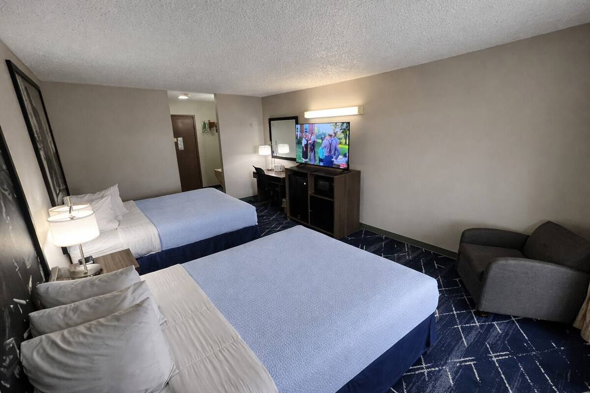 Une chambre d’hôtel avec deux lits, un bureau, une chaise, une télévision et un miroir.