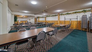Une salle de conférence dotée de plusieurs tables et chaises, de murs recouverts de panneaux en bois et d’un ventilateur de plafond.