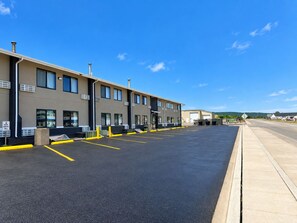A parking lot with a row of buildings, a clear sky, and a distant view of a hilly landscape. - Super 8 by Wyndham Sturgis (Sturgis)