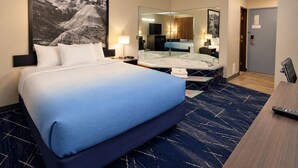 A hotel room with a large bed, a sitting area with a desk, a mirror, and a bathroom with a bathtub.