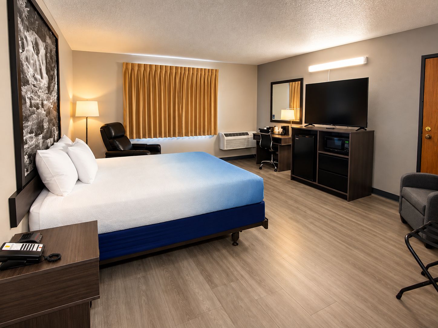 A hotel room with a bed, desk, chair, TV, and a minibar.