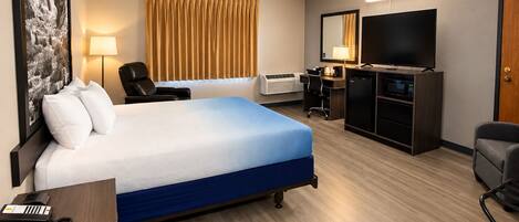 Habitación de hotel con cama, escritorio, silla, televisión y minibar.