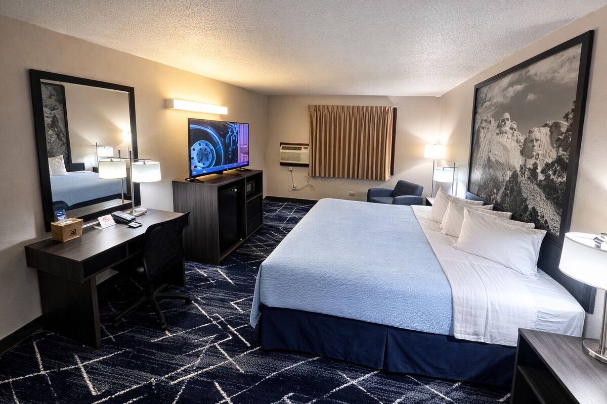 Une chambre d’hôtel avec un lit, un bureau, une télévision et un grand tableau au mur.