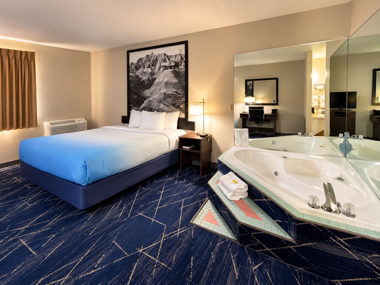 Habitación de hotel con cama, un espejo grande, una bañera y un escritorio con lámpara.