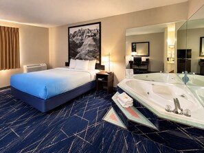A hotel room with a bed, a large mirror, a bathtub, and a desk with a lamp.