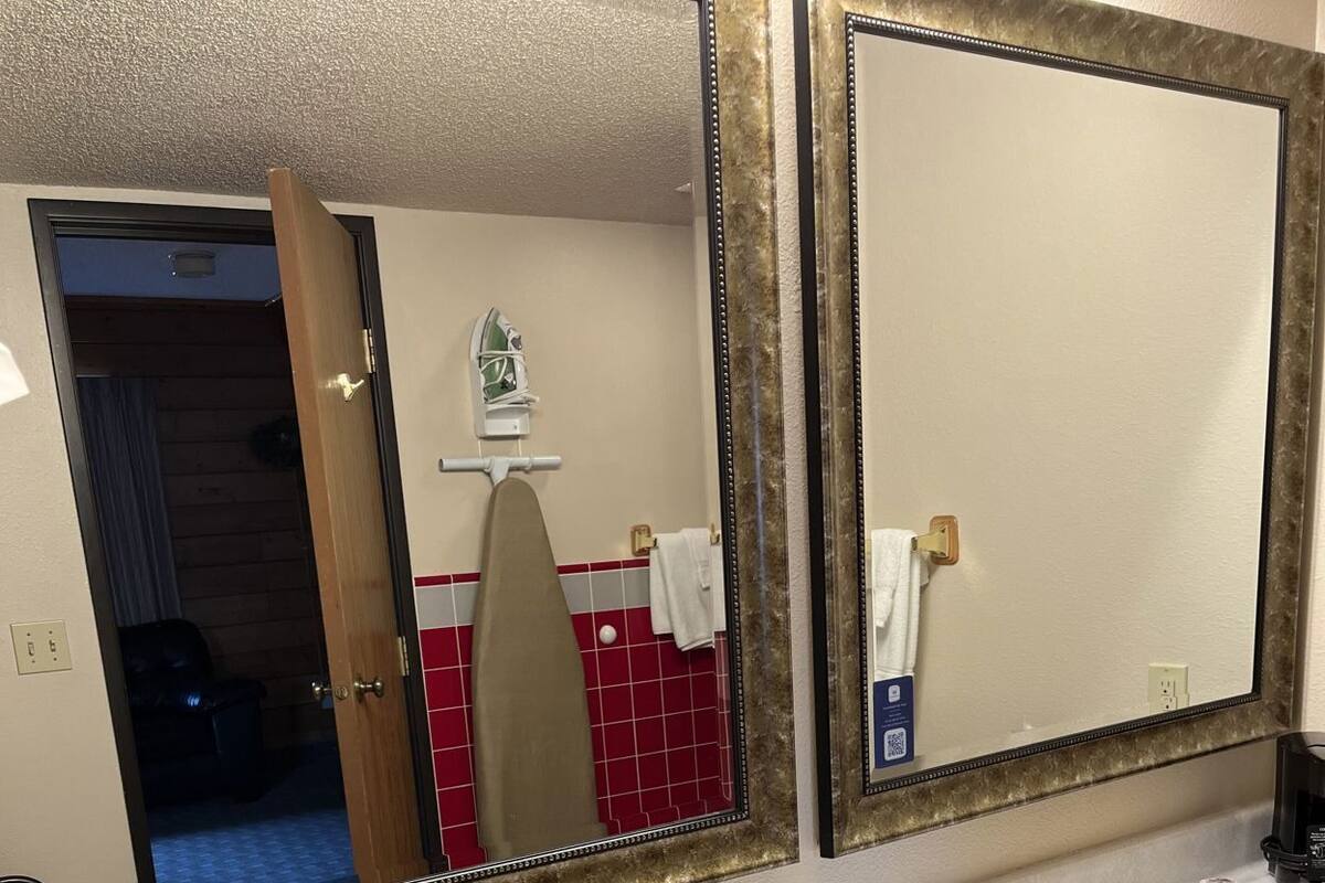 Une salle de bain d’hôtel avec deux lavabos, un miroir et une porte donnant sur une autre pièce.