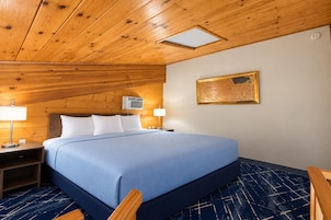 Habitación de hotel con techo de madera, cama con cubrecama azul, dos lámparas de noche y un equipo de aire acondicionado instalado en la pared.