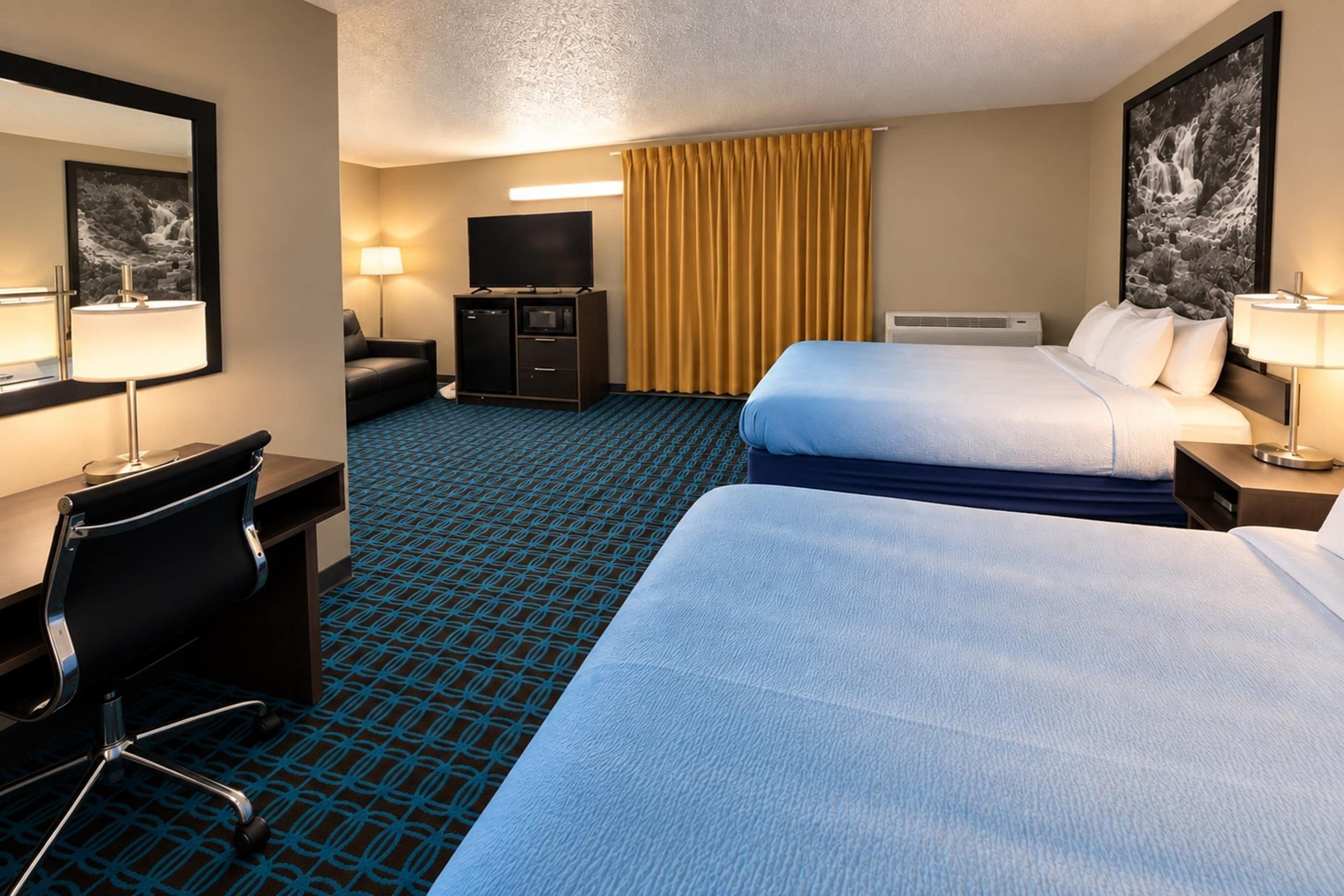 Une chambre d’hôtel avec deux lits, un bureau avec une chaise, une télévision et un minibar.